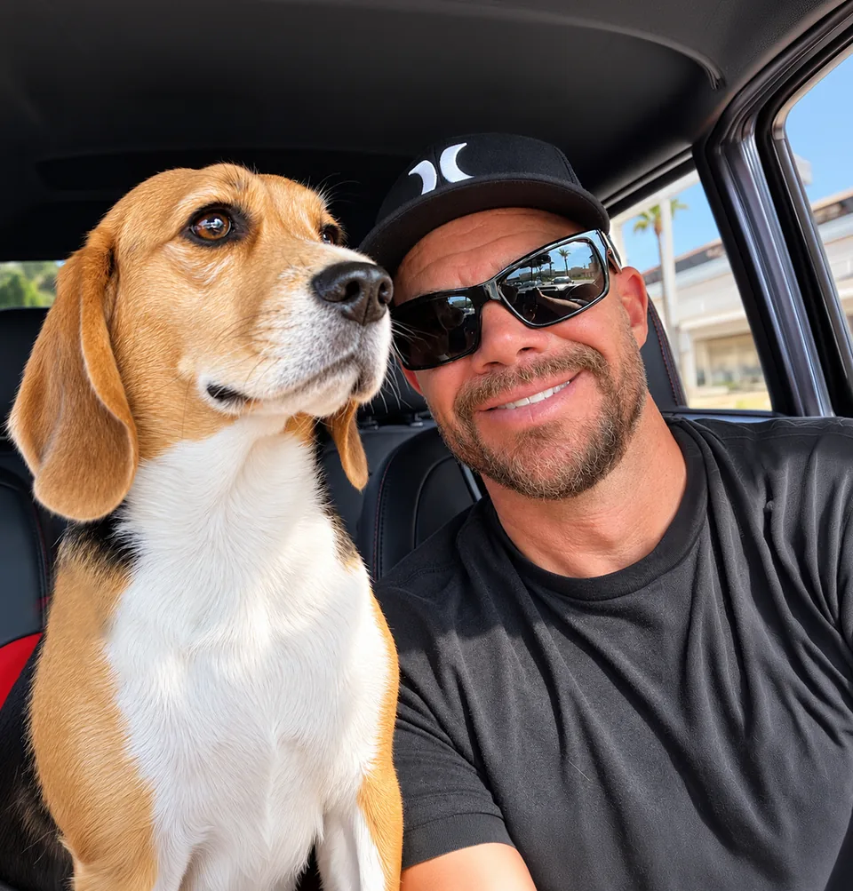James in a black cap and sunglasses smiling beside Sunny, a tricolor Beagle, in the front seat of a car